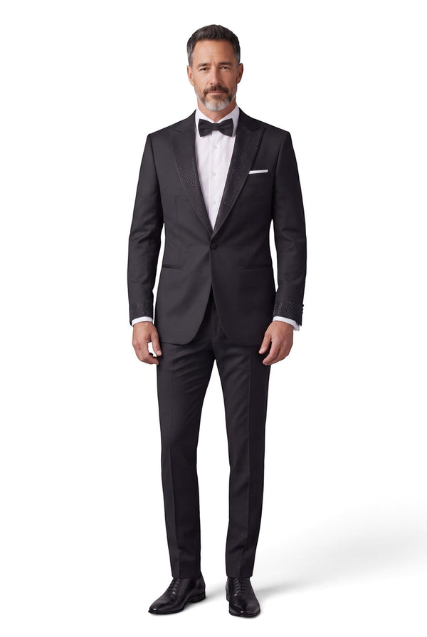 A man wearing a Cosiani black tuxedo with crystal-embellished lapels and cuffs, paired with a white shirt and bow tie.